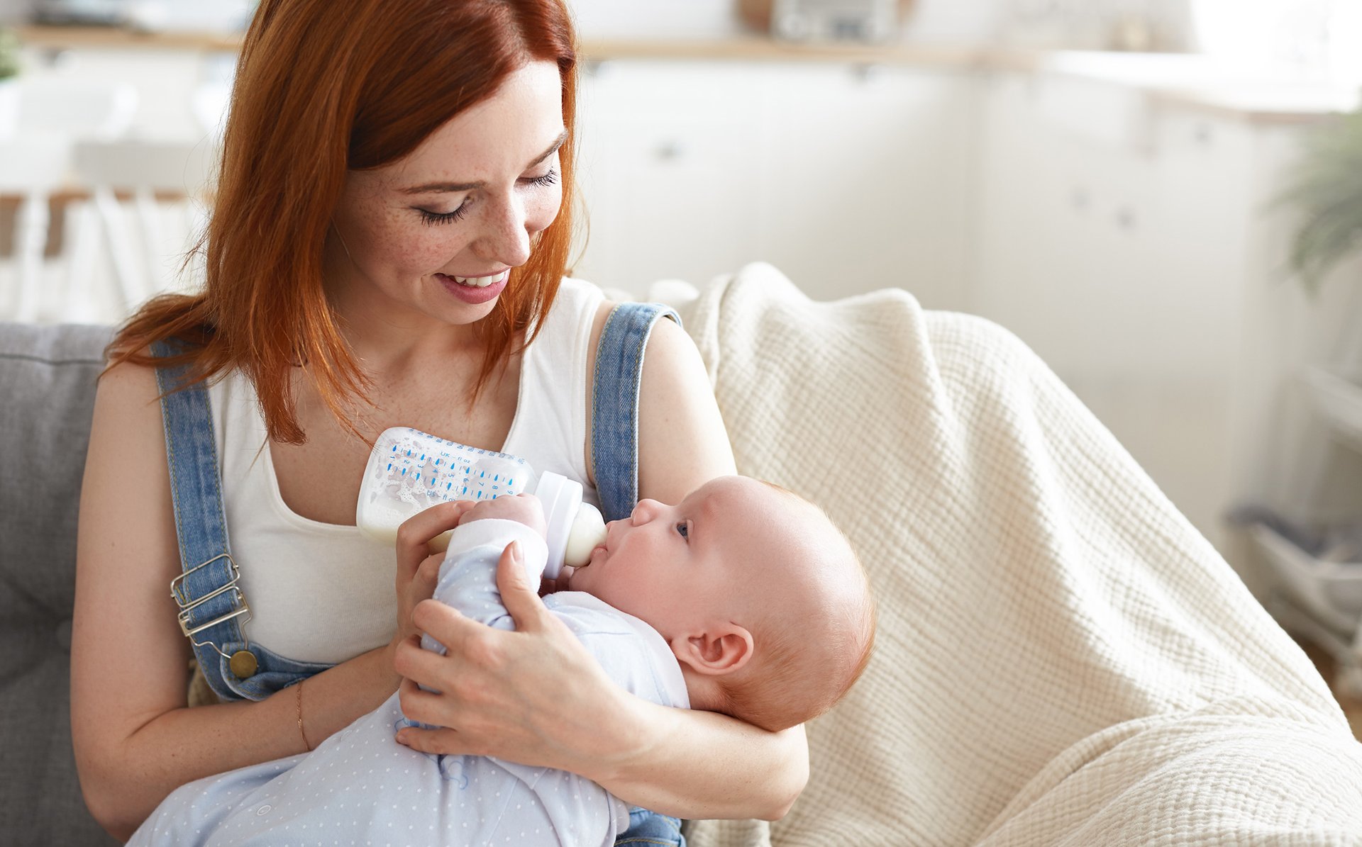 Mama w ogrodniczkach karmi dziecko butelka