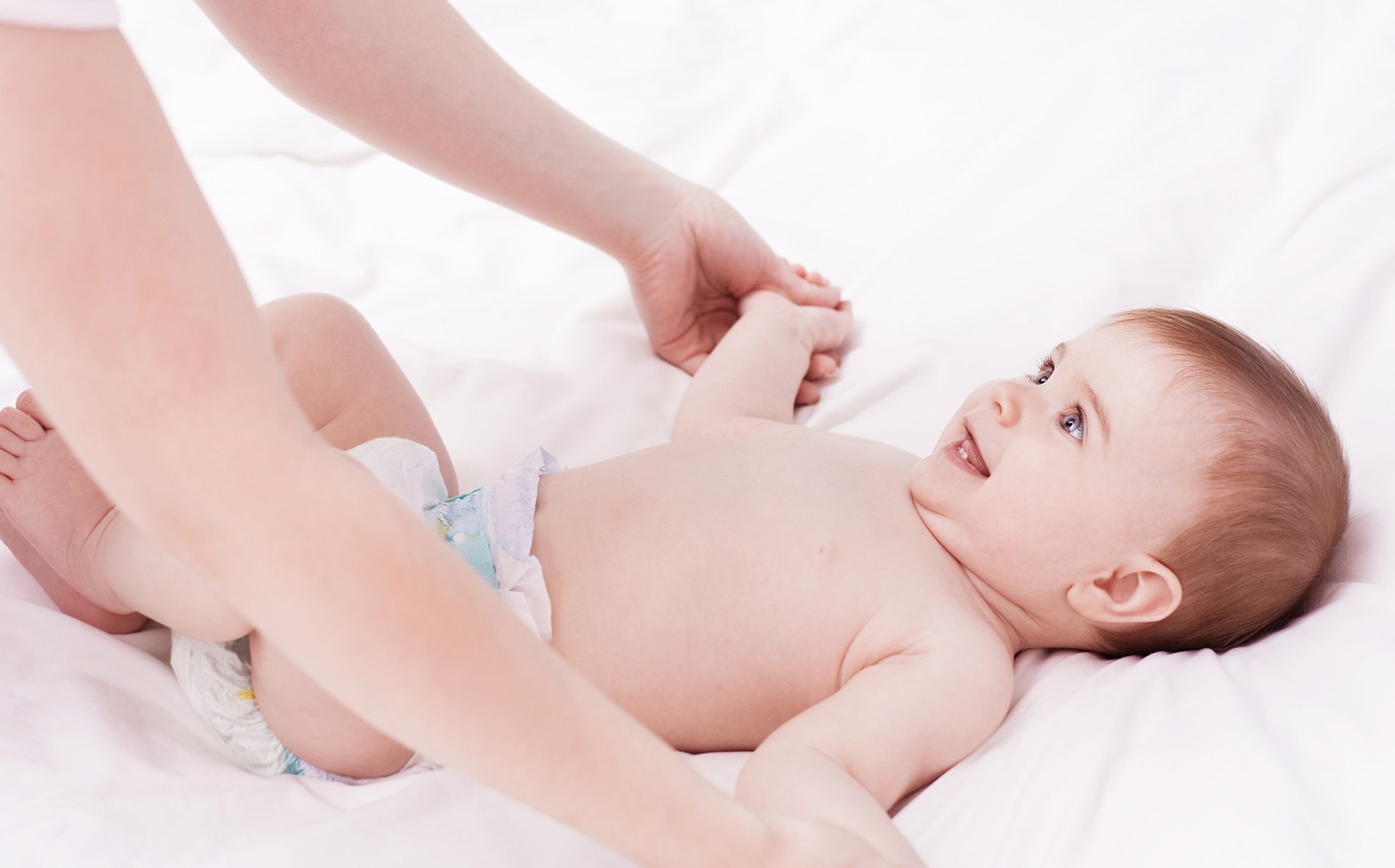 Mama trzyma za rece male dziecko lezace na lozku