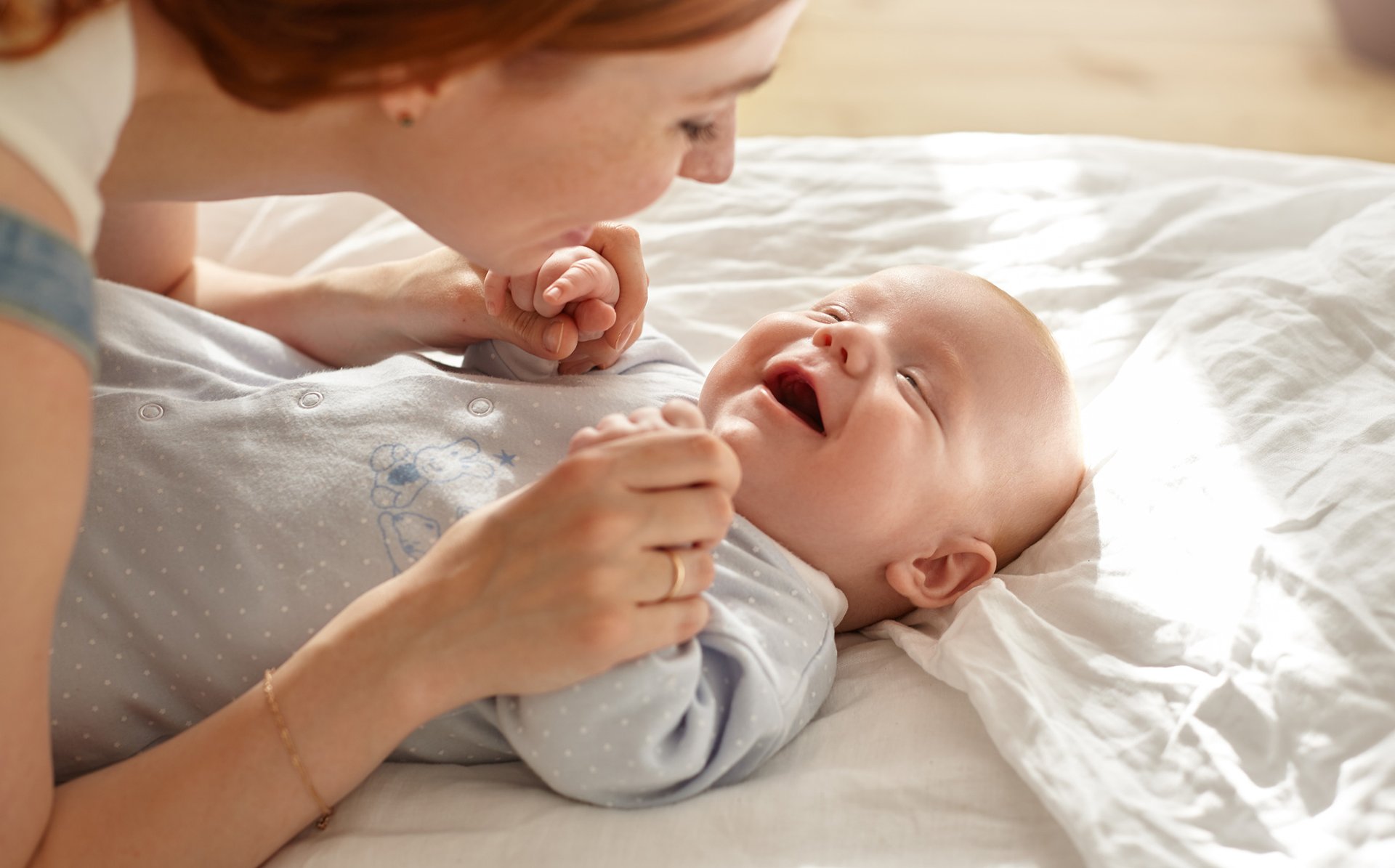 Mama usmiecha sie do dziecka trzymajac je za raczki