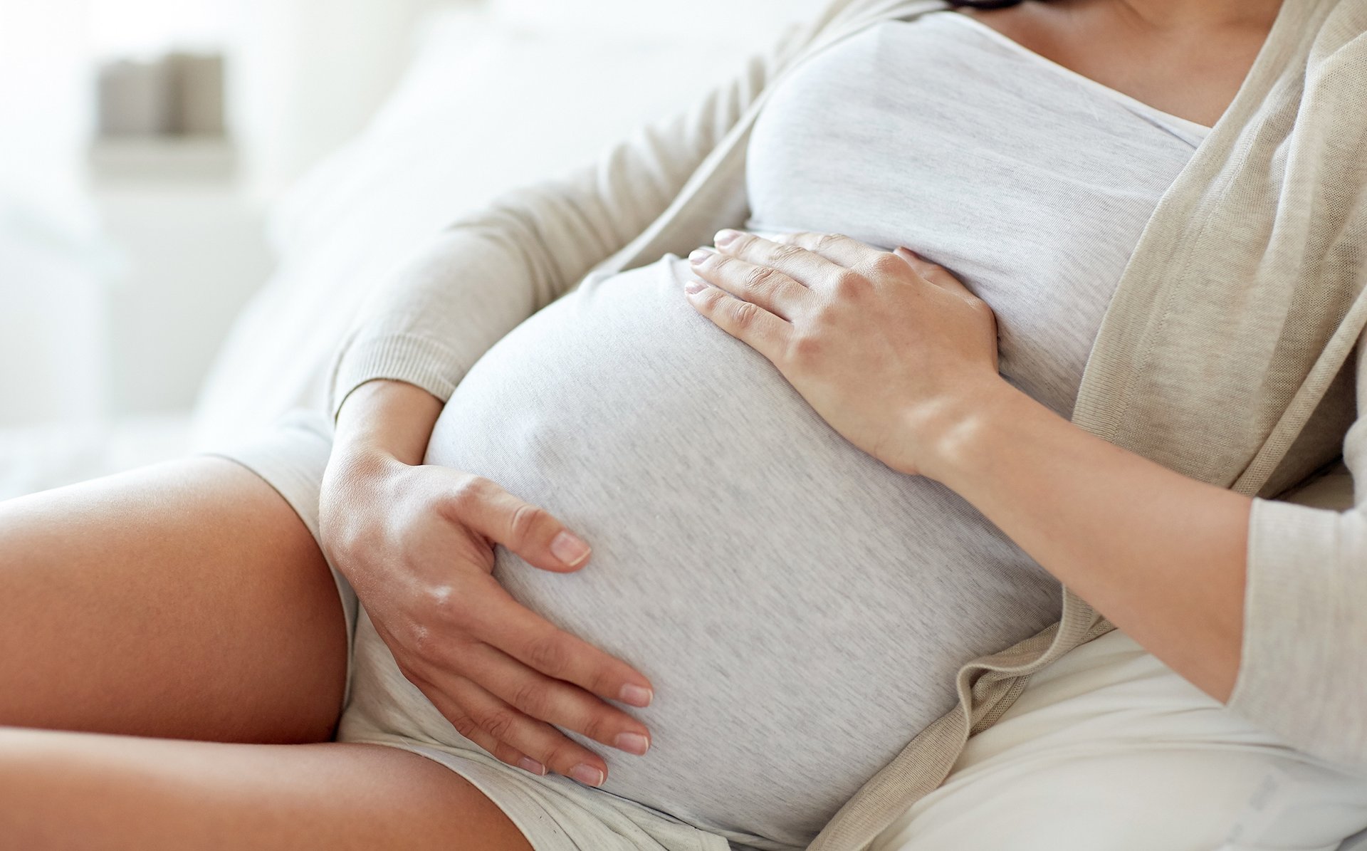 Kobieta lezy na poduszkach trzymajac sie za ciazowy brzuch