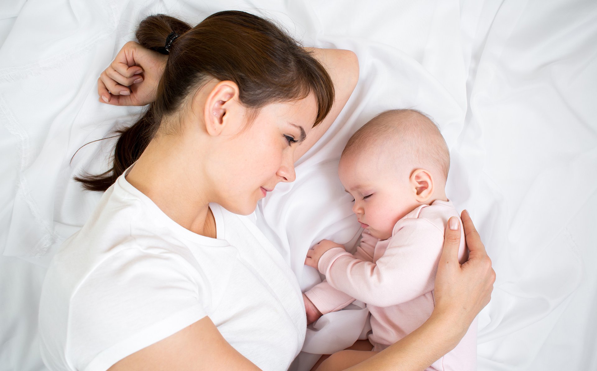 Mama spi z dzieckiem na bialej poscieli