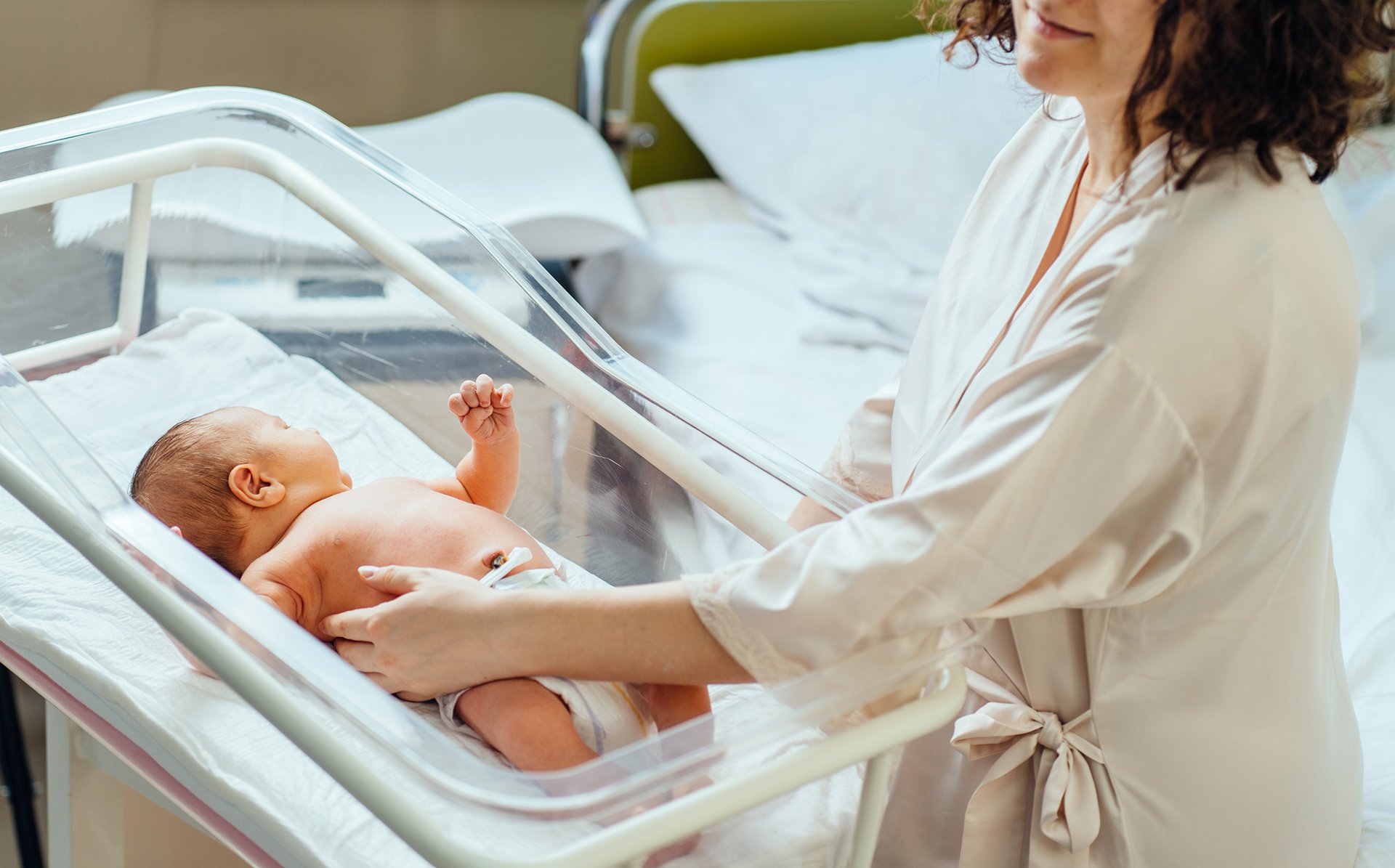 Mama glaszcze dziecko lezace w szpitalnym lozeczku